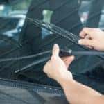 A person is replacing the windshield wipers on a car after visiting a used car dealer in Albany.