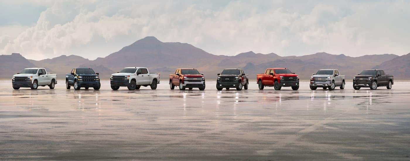 A row of 2021 Chevy Silverado 1500s are shown parked on a landing strip in front of a mountain.