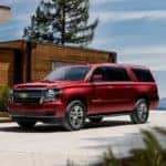 A red 2020 Chevy Suburban is shown parked outside of a modern home after visiting a Clifton Park used car dealer.
