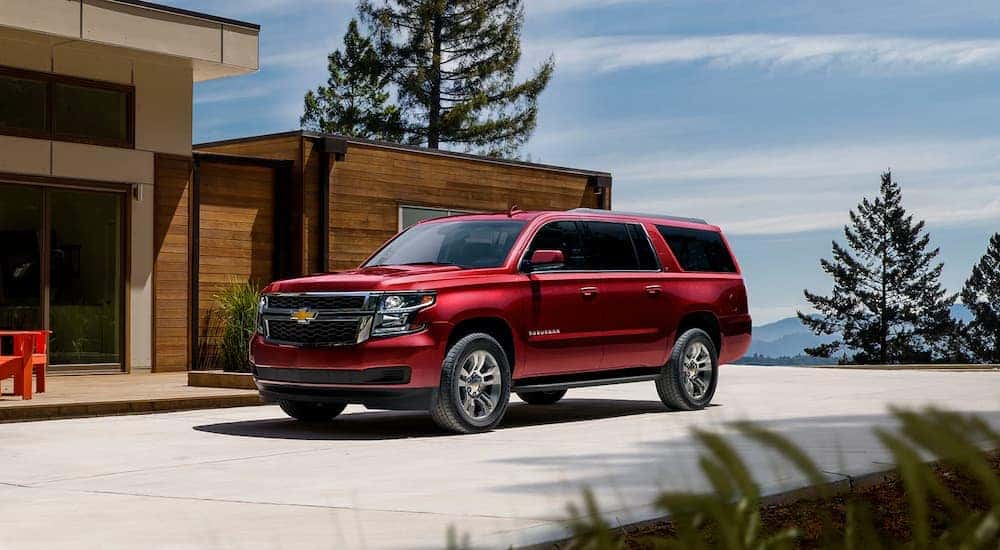 A red 2020 Chevy Suburban is shown parked outside of a modern home after visiting a Clifton Park used car dealer.