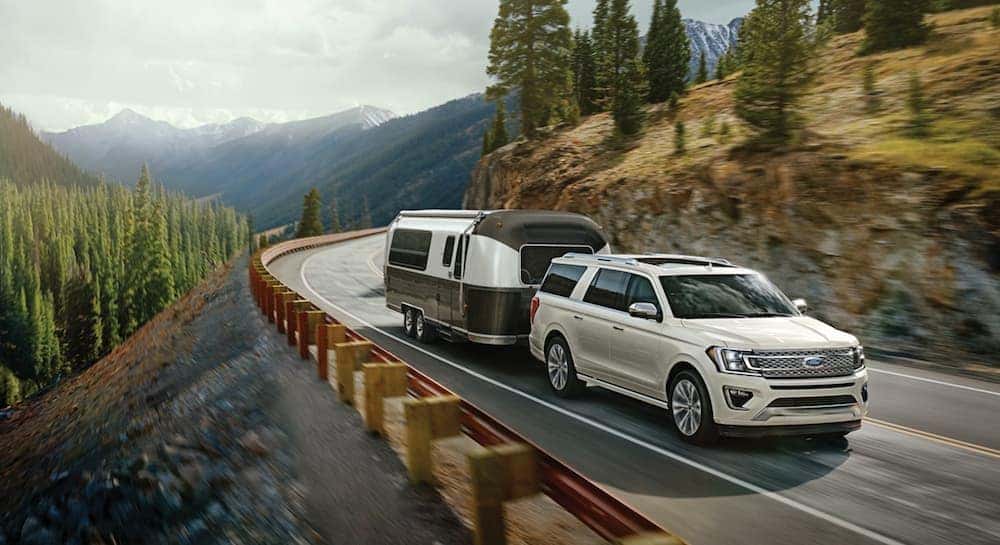 A white 2020 Ford Expedition is shown towing a camper through the mountains.