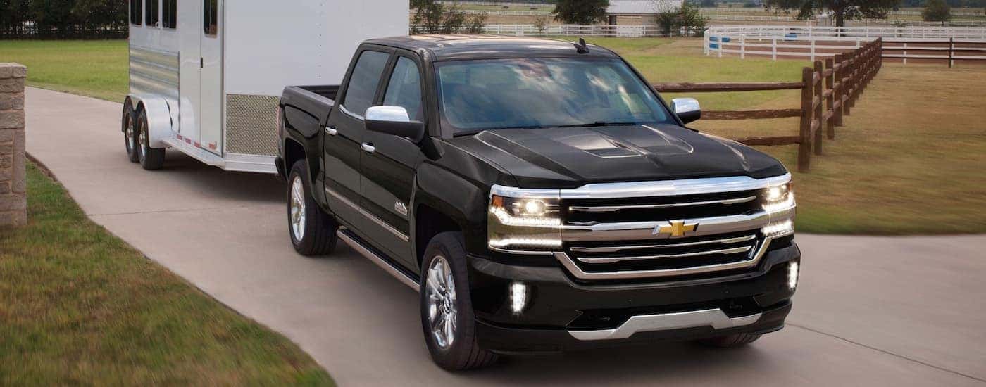 A black 2018 Chevy Silverado 1500 is shown towing a white horse trailer.