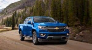 A blue 2020 Chevy Colorado is shown from the front driving on a dirt road.