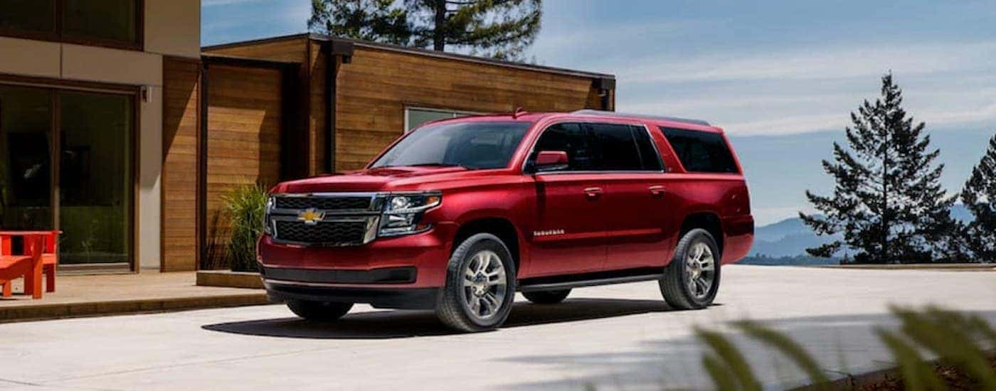 A red 2020 Chevy Suburban is shown from the front parked at a modern home in the mountains after looking at Albany Certified Pre-Owned cars.