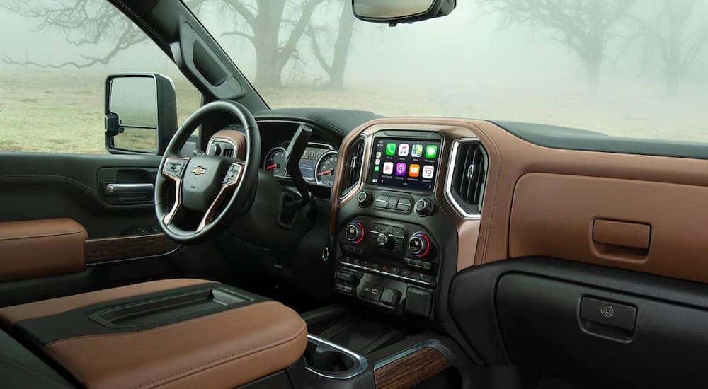 The black and tan interior of a 2021 Chevy Silverado 1500 shows the steering wheel and infotainment screen.