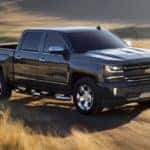 A black 2018 Chevy Silverado 1500 is shown driving through a dry grassy field.