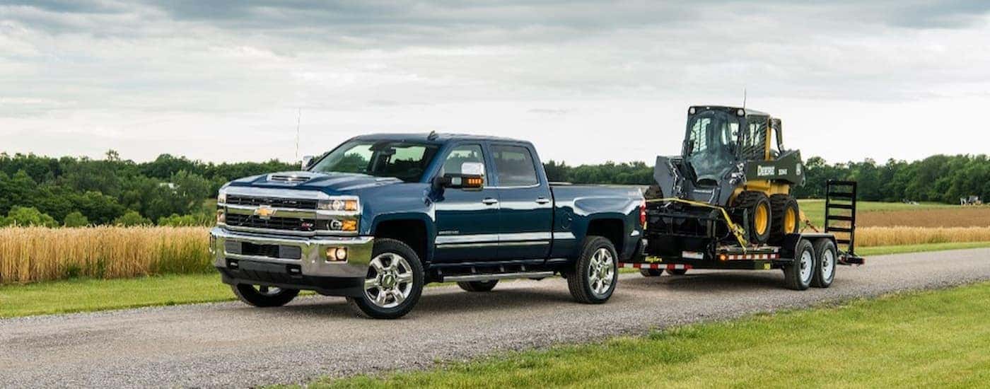A blue 2018 Chevy Silverado 2500HD is shown towing heavy machinery.
