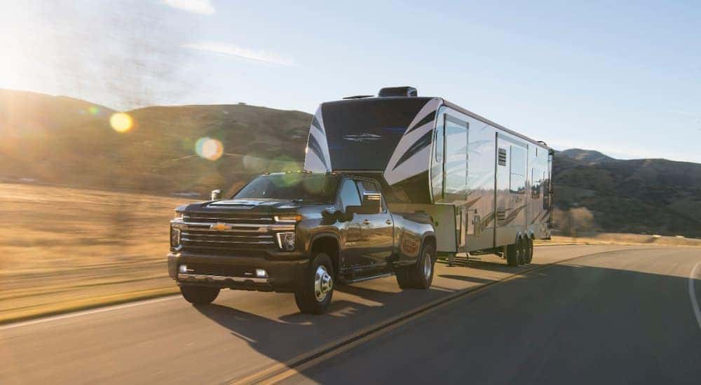 A black 2020 Chevy Silverado 3500HD is shown towing a camper after leaving a used Chevy Silverado dealership.