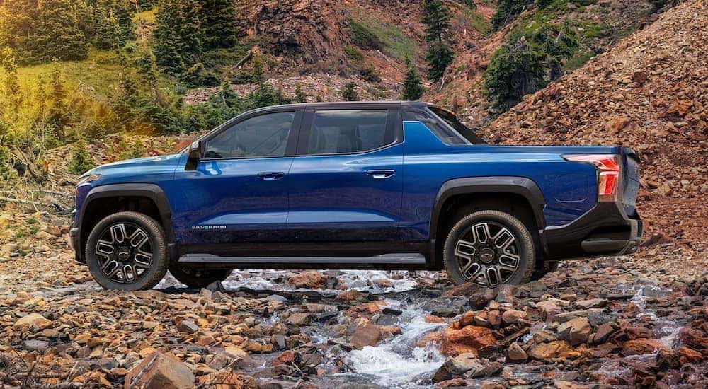 Side view of a blue 2024 Chevy Silverado EV driving over a creek after visiting a Albany Chevy Silverado dealer