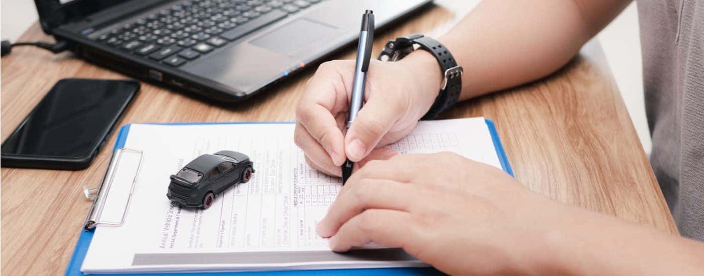 A person is shown filling out paperwork in preparation for selling their car.