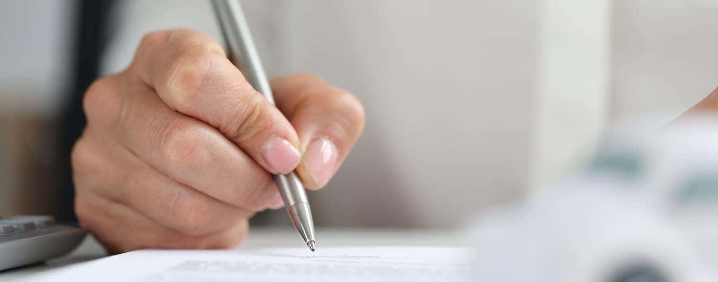 A close up shows a person signing a car lease.
