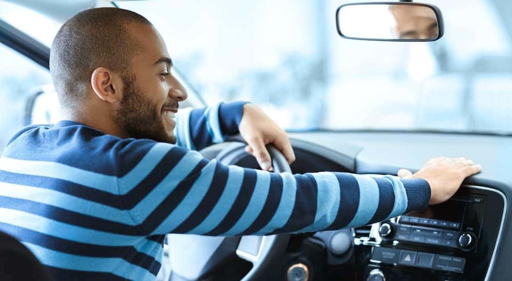 A person in a striped shirt is shown sitting in the drivers seat of a car after searching 'sell my car.'
