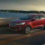 A red 2017 Ford Escape is shown from the side driving on an open road past a body of water.
