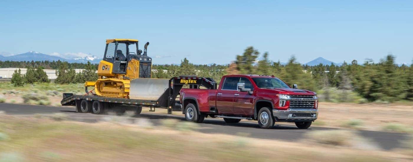 A red 2022 Chevy Silverado 3500HD is shown towing heavy machinery on an open road.