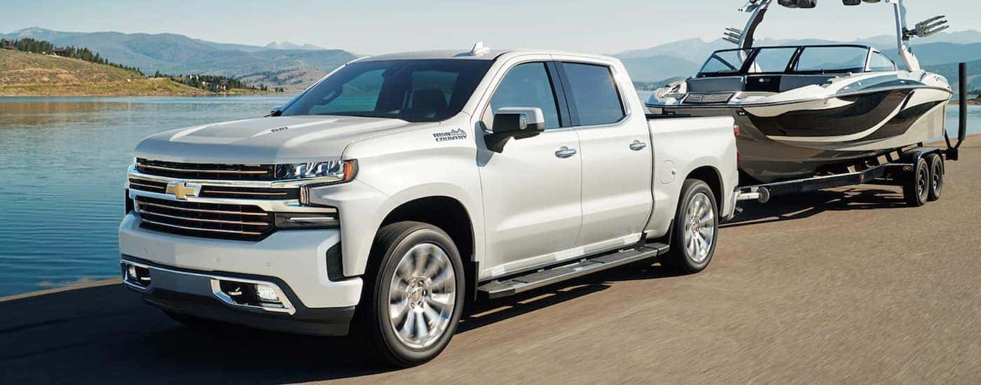 A white 2022 Chevy Silverado 1500 High Country is shown towing a boat.