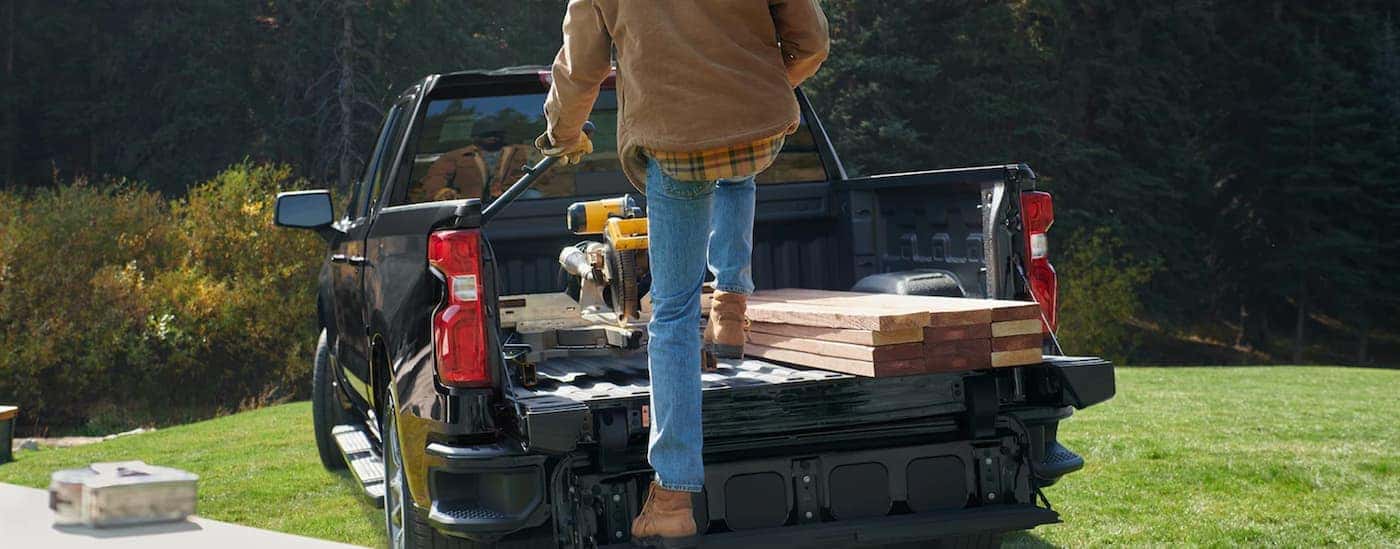 A black 2022 Chevy Silverado 1500 is shown from the rear as a man loads the bed with tools.