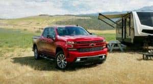 A red 2022 Chevy Silverado 1500 is shown from the front parked in an open field next to a camper.