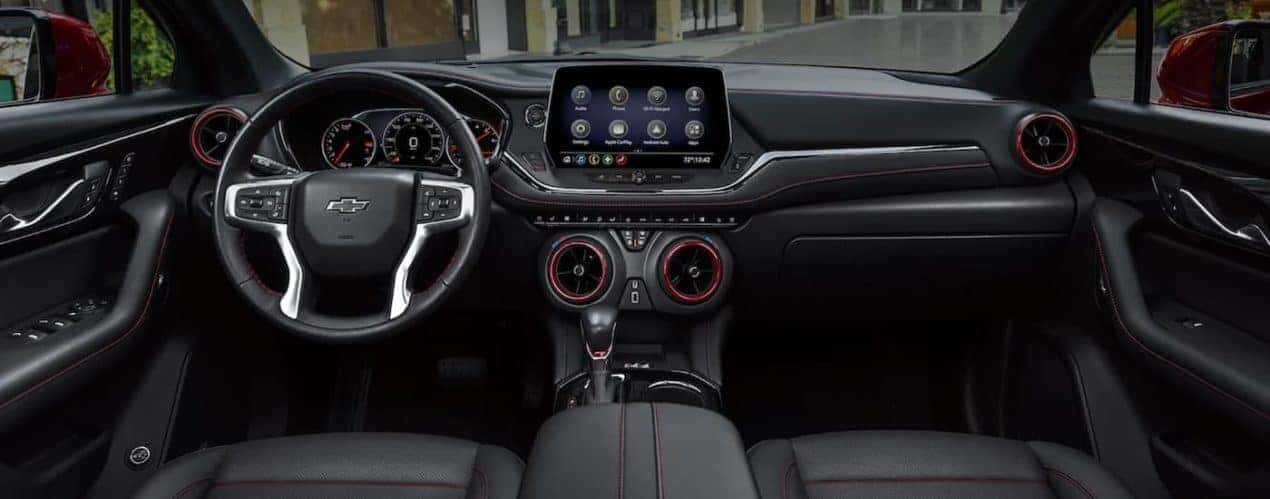 The black and red accented interior of a 2022 Chevy Blazer shows the steering wheel and infotainment screen.