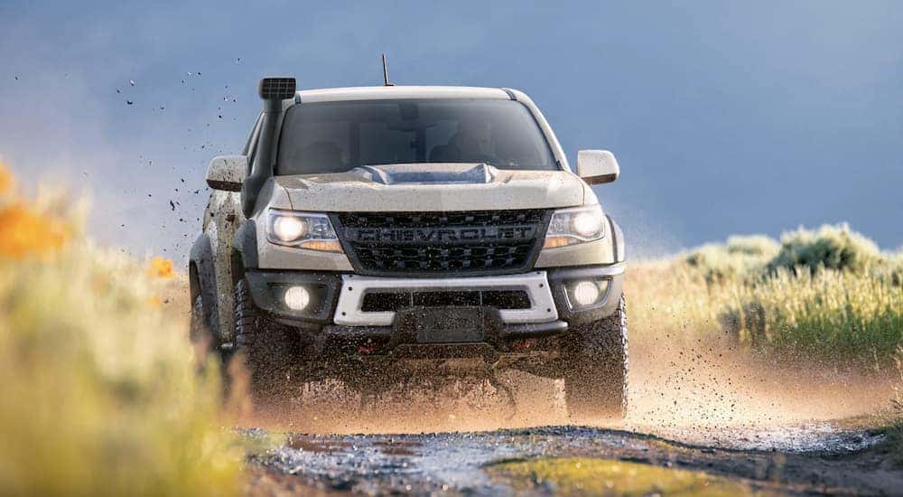 A tan 2022 Chevy Colorado ZR2 is shown from the front off-roading on a muddy path.