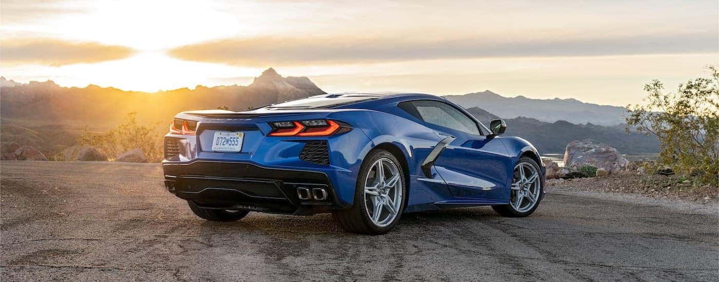 A blue 2022 Chevy Corvette Stingray is shown from the rear in an empty lot overlooking mountains.