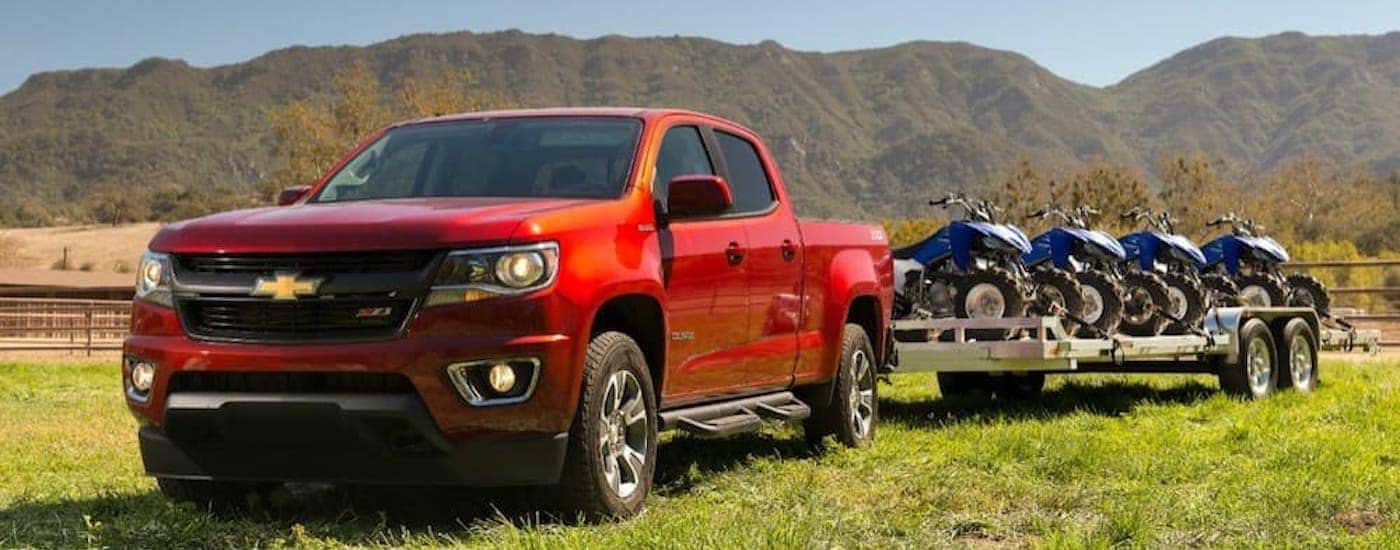 A red 2018 Chevy Colorado is shown towing a trailer full of ATVs.