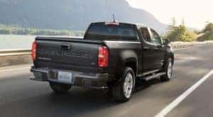 A black 2022 Chevy Colorado is shown from the rear driving on an open road after leaving a small pickup dealership.