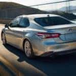 A silver 2020 Toyota Camry XLE Hybrid is shown from the rear driving on an open road.