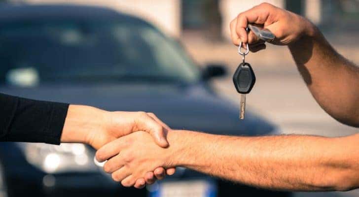 A salesperson is shown shaking hands with a car buyer at a Troy used car dealership.