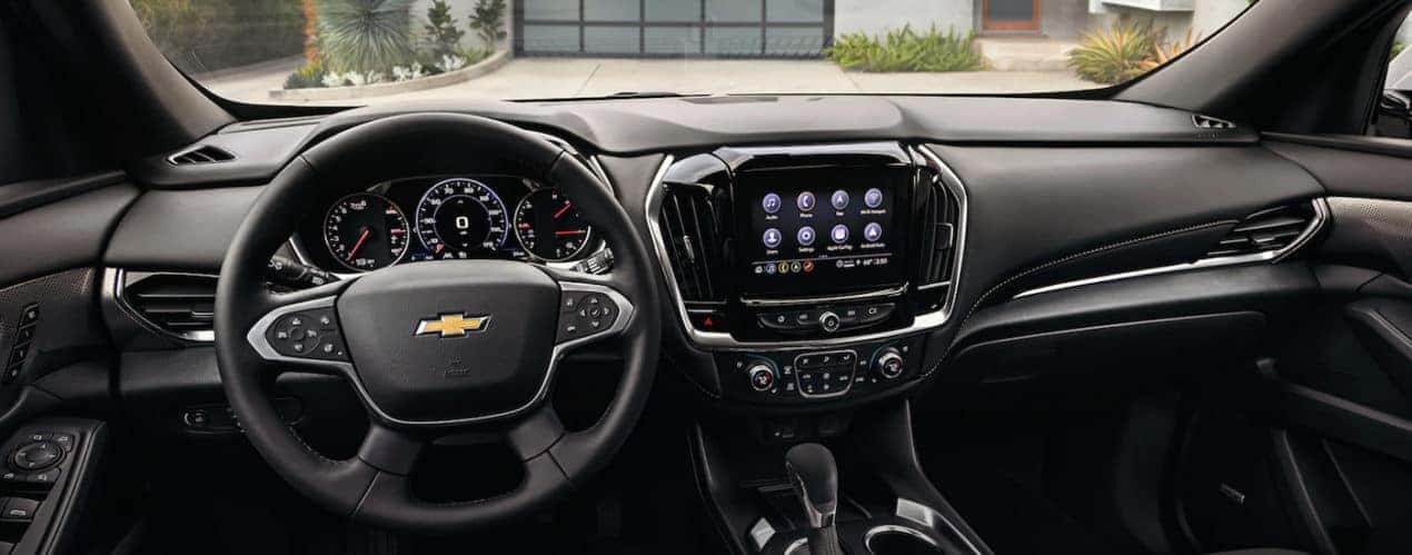 The black interior of a 2022 Chevy Traverse shows the steering wheel and infotainment screen.