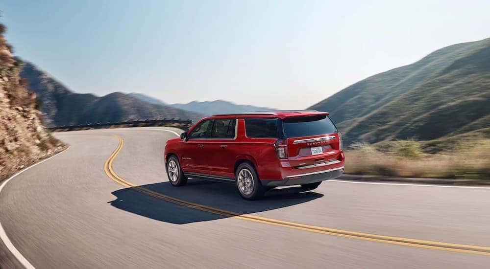 A red 2022 Chevy Suburban is shown from the rear driving on a road after leaving one of the best Albany, NY Chevy dealers.