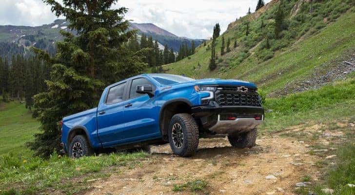 A blue 2022 Chevy Silverado 1500 ZR2 is shown driving up a dirt trail after leaving an auto dealer in Clifton Park.