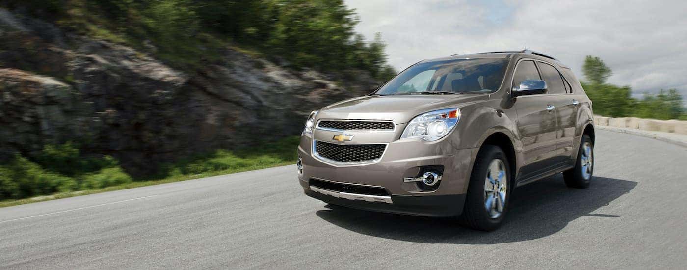 A tan 2013 Chevy Equinox LTZ is shown driving past a rock feature.