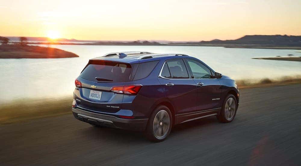 A blue 2022 Chevy Equinox Premier is shown driving past a lake after leaving a Chevy Equinox dealer.