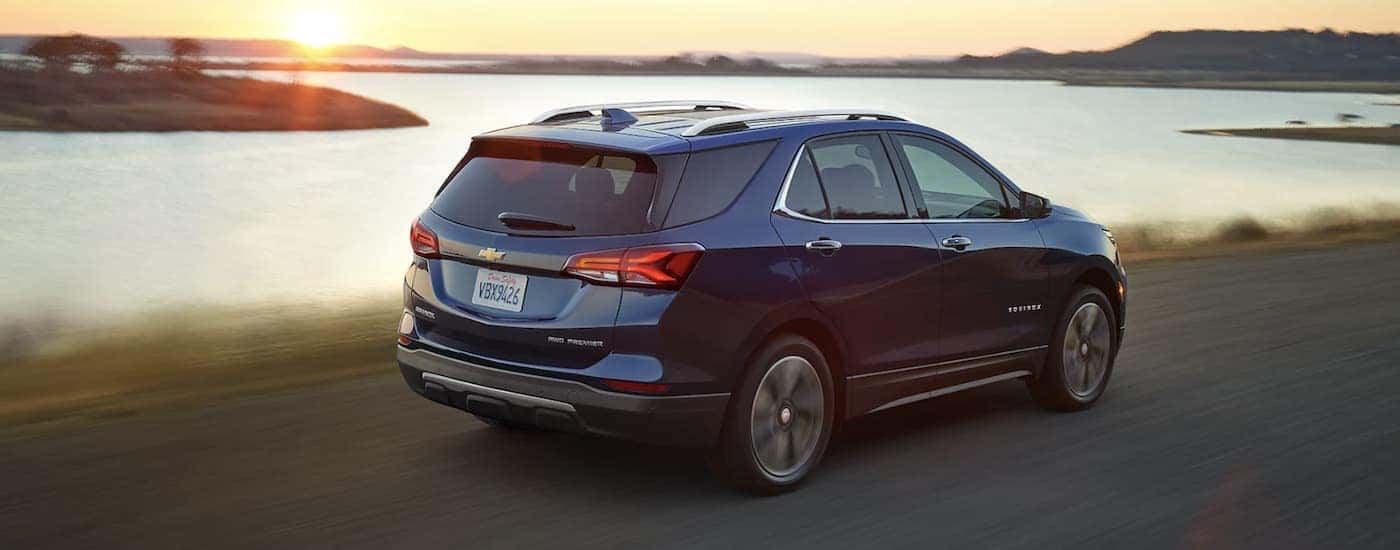 A blue 2022 Chevy Equinox is shown from the rear driving past a body of water.