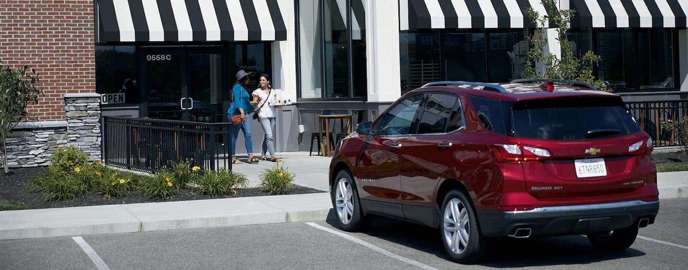 A maroon 2020 Chevy Equinox Premier is shown from the rear parked in front of a shop.