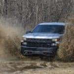 A silver 2022 Chevy Silverado 1500 Trail Boss is shown from the front while driving through mud.