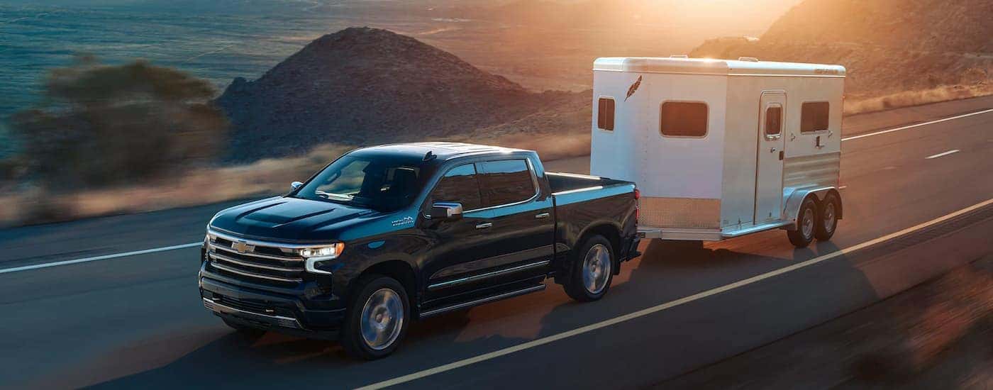 A black 2022 Chevy Silverado High Country is shown towing a white enclosed trailer on an open road.