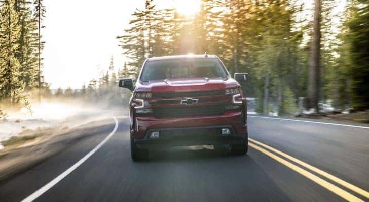 A popular used Chevy near you, a red 2020 Chevy Silverado 1500, is shown driving on a tree-lined road.