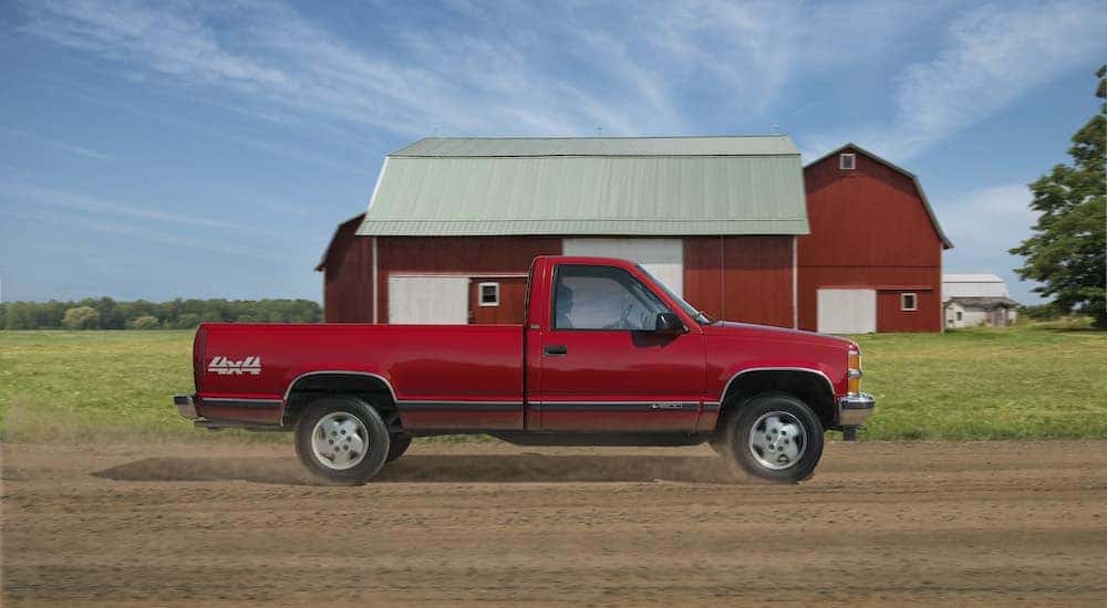A red 1988 Chevy GMT40 is shown driving past a red barn.