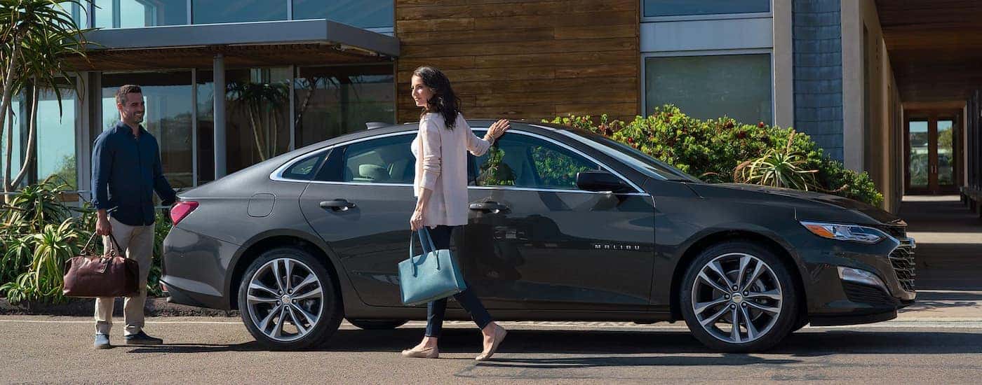 A grey 2023 Chevy Malibu is shown from the side parked in front of a hotel.
