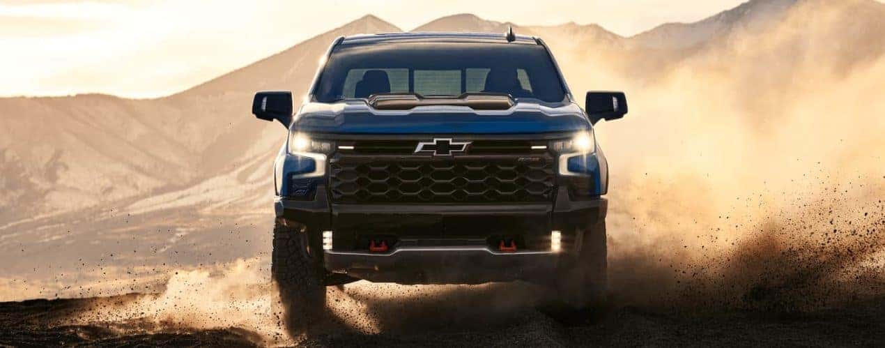 A blue 2023 Chevy Silverado 1500 ZR2 is shown from the front driving on a dusty path.