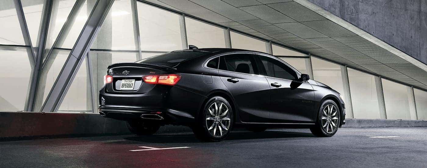 A black 2023 Chevy Malibu RS is shown from the side parked next to a building with lots of windows.