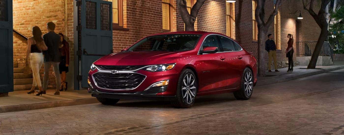 A red 2023 Chevy Malibu is shown parked on the side of a street near a restaurant.