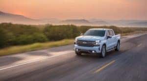 A white 2020 Chevy Silverado 1500 is shown driving on an open road after leaving a certified used truck dealer.