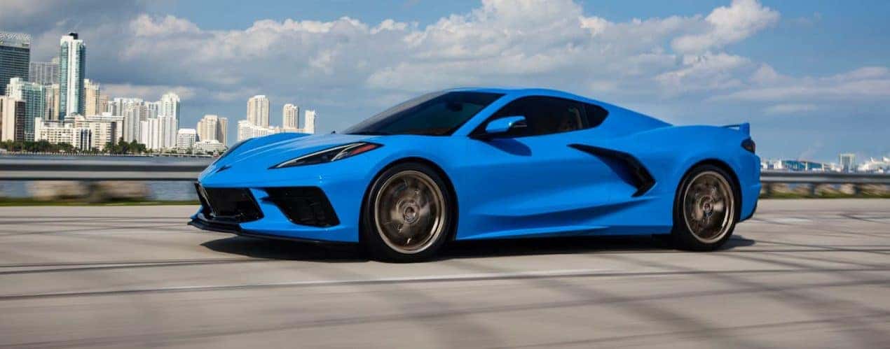 A blue 2023 Chevy Corvette 3LT is shown driving past a river and a city.