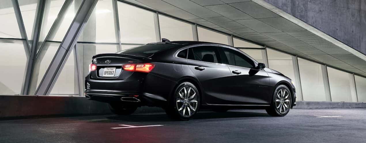 A black 2023 Chevy Malibu RS is shown from a rear angle parked next to a row of windows.
