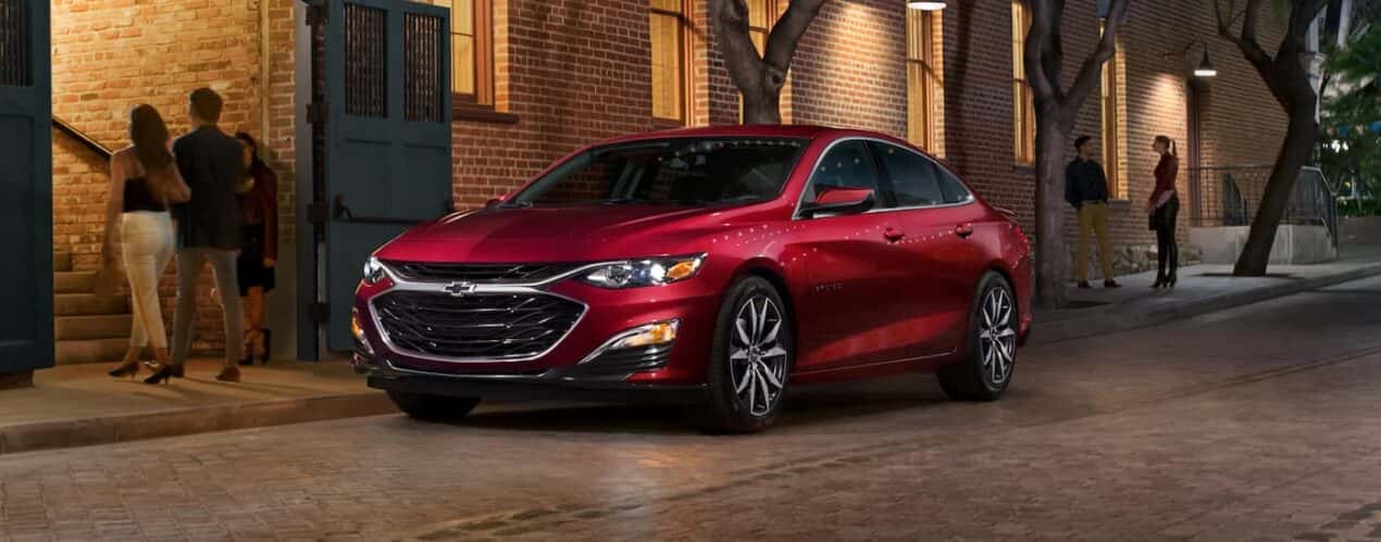 A red 2023 Chevy Malibu is shown parked on the side of a city street.