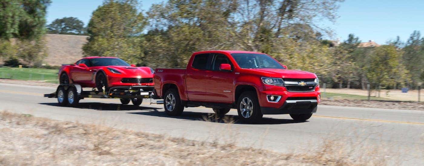 A red 2018 Chevy Colorado is shown towing a red 2018 Chevy Corvette on a trailer on an open road.