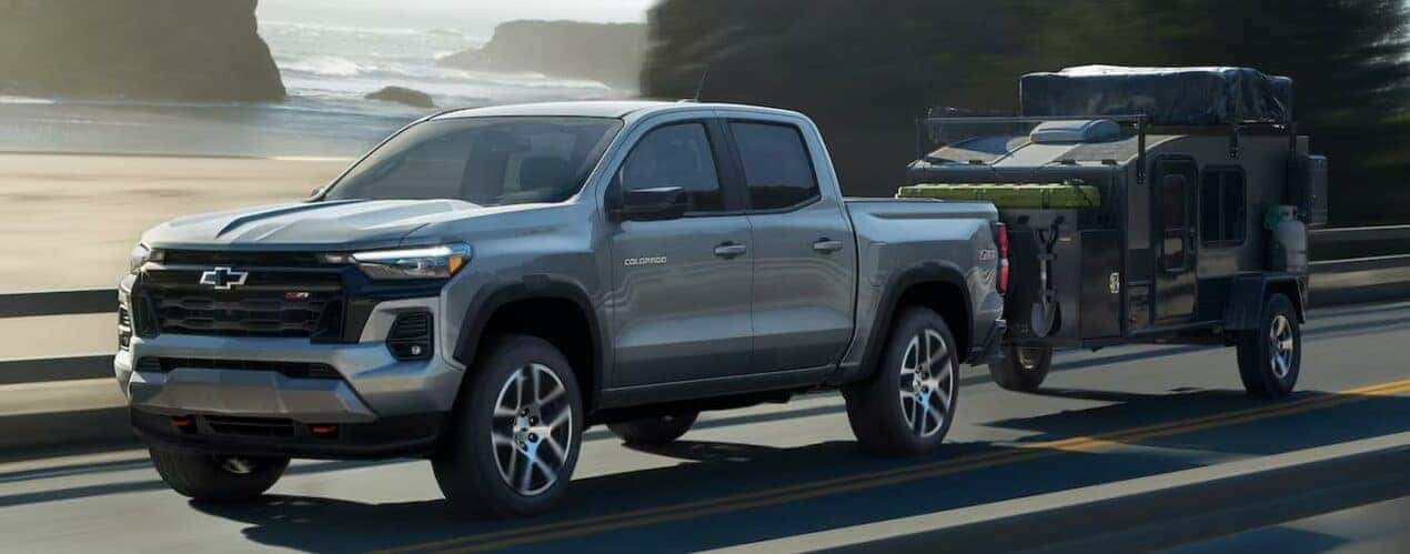 A silver 2023 Chevy Colorado Z71 is shown towing a small trailer on an open highway.