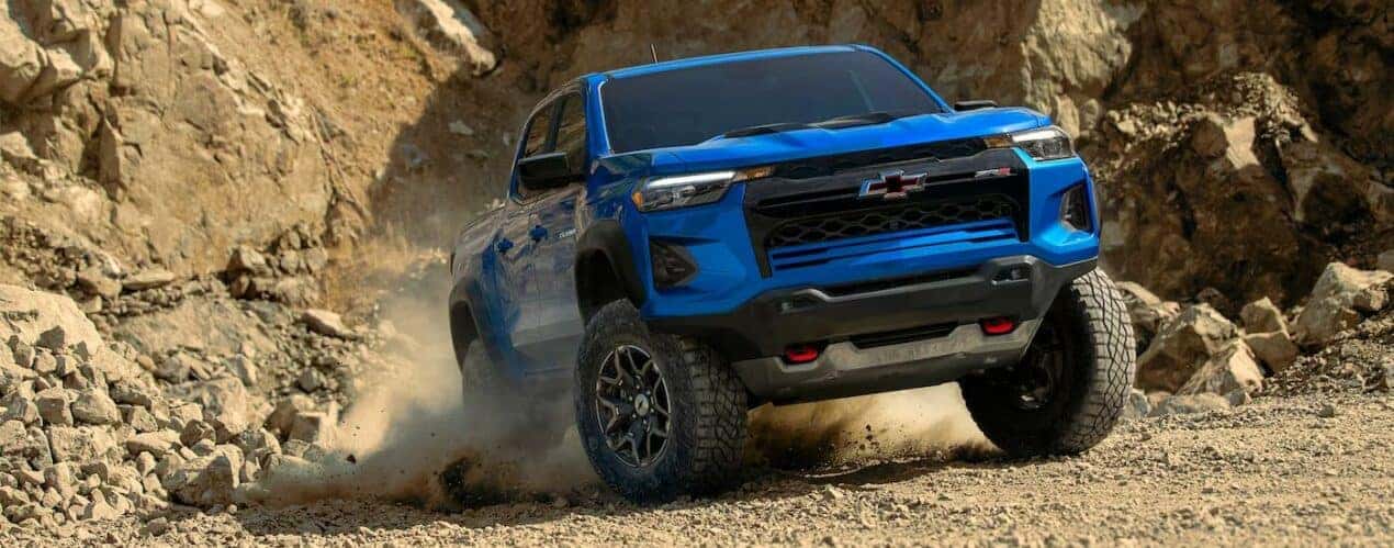 A blue 2023 Chevy Colorado ZR2 is shown off-roading on a dusty trail after a 2023 Chevy Colorado vs 2023 Ford Ranger comparison.